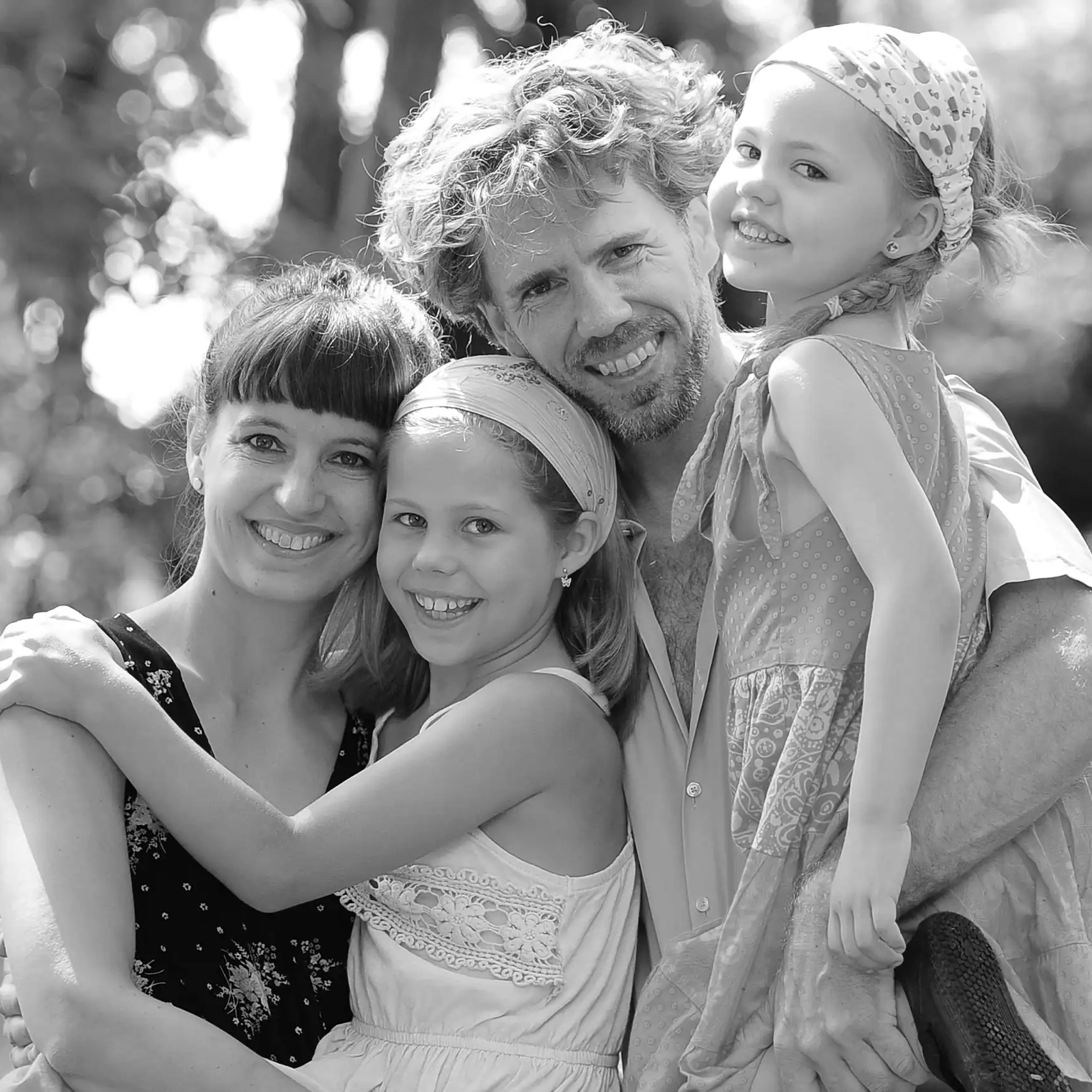 Familienportrait in schwarz-weiß im Grünen mit schönem unscharfem Hintergrund, mit zwei Mädchen, Mamma und Papa lachen in die Kamera.
