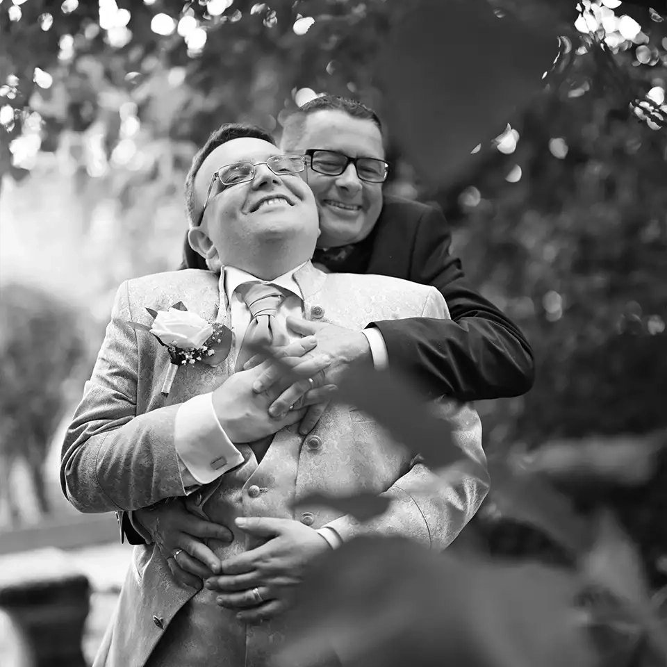 Gleichgeschlechtliches Hochzeitspaar im Park, herzliche Umarmung unscharfe Blätter.