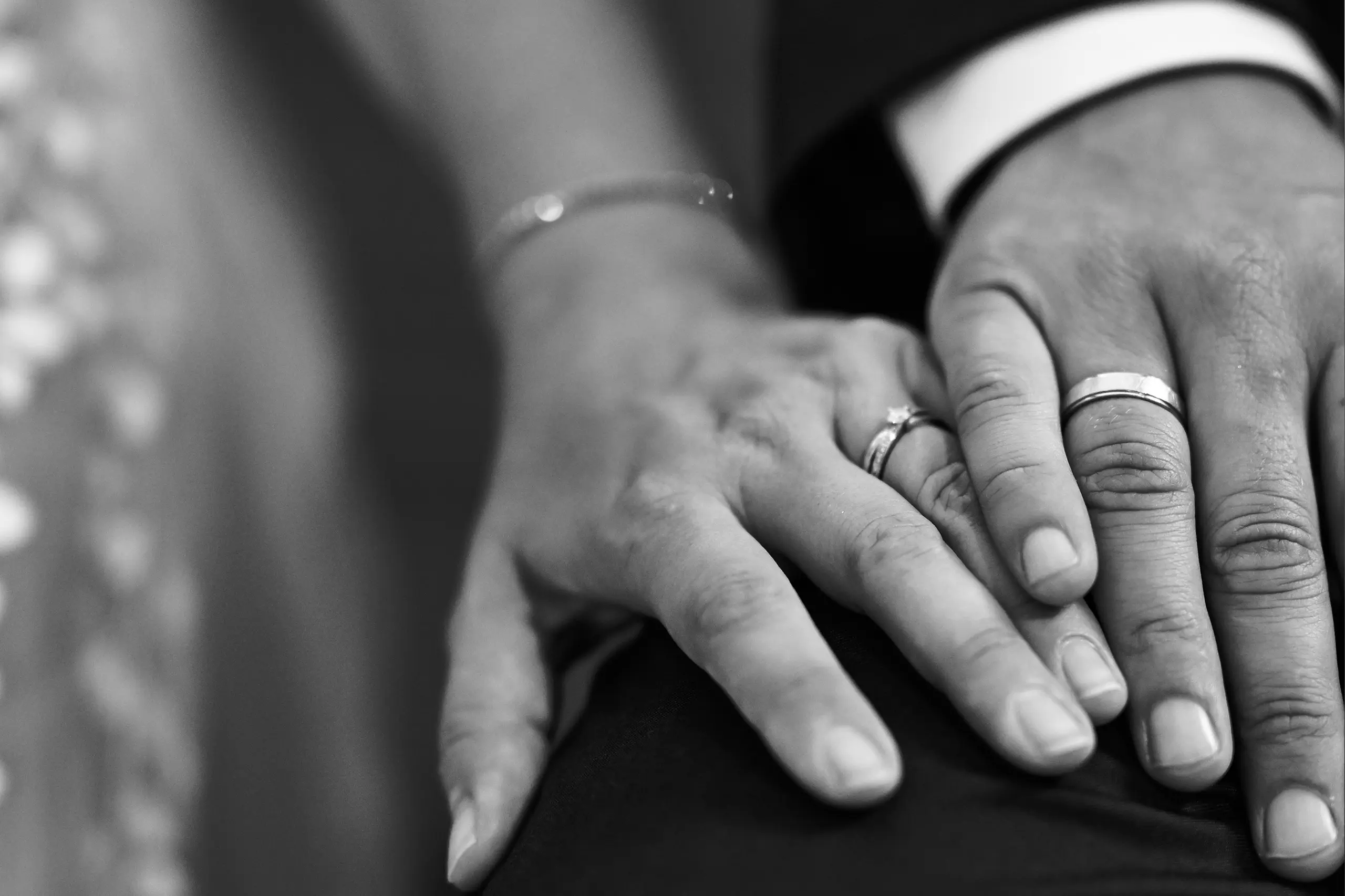 Schwarz-weiß Foto der sich berührenden Hände des Hochzeitpaares mit Ringen.