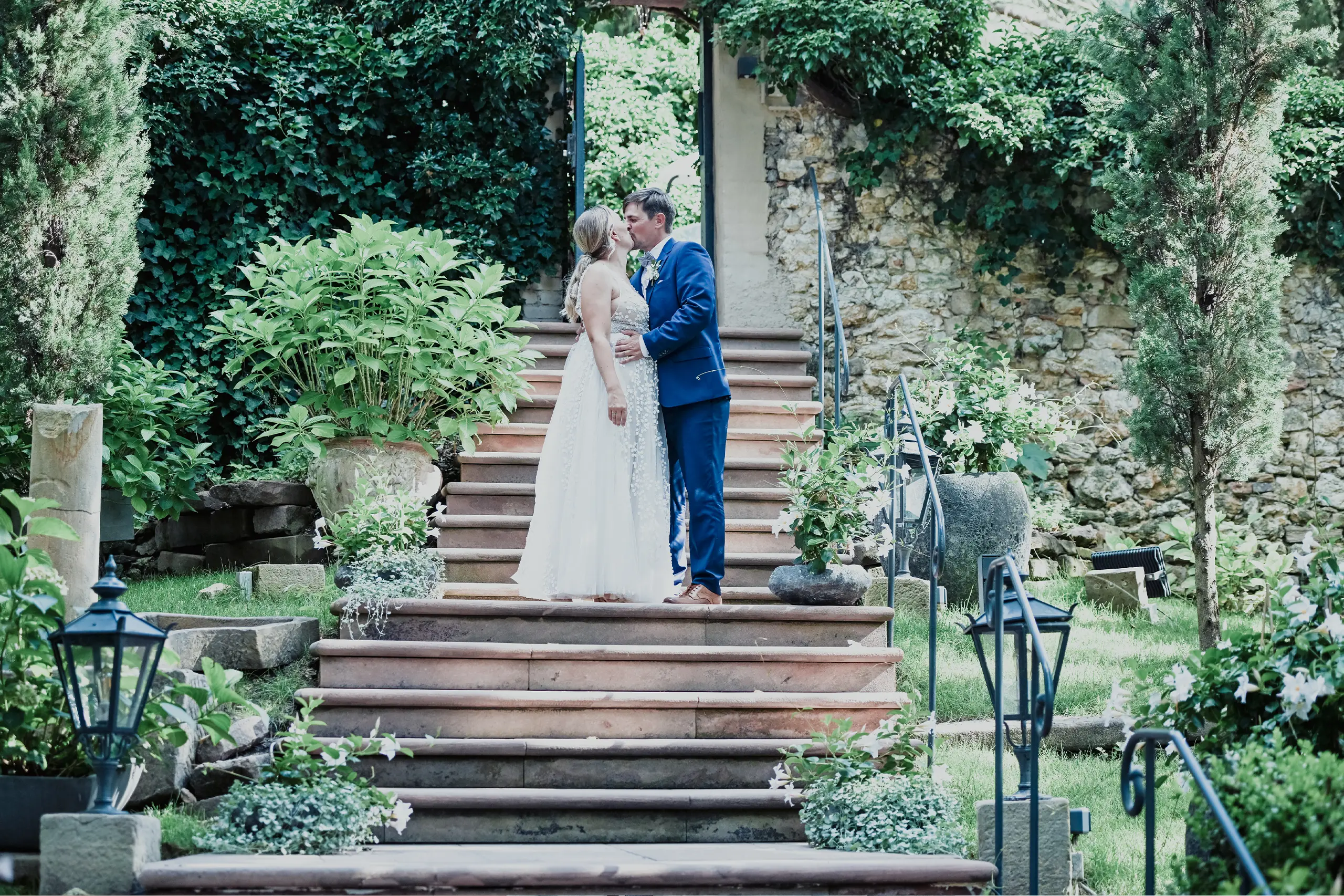 Foto eins Hochzeitpaares das küssend auf eine Treppe steht im wunderschönen Park.
