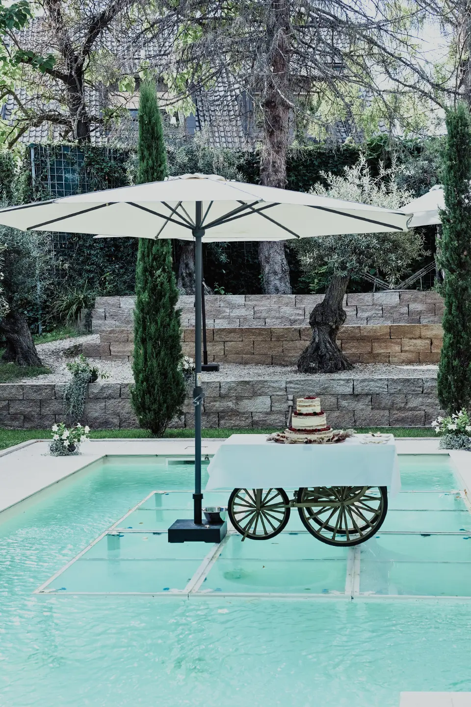 Hochzeitstorte auf einem Wagen der auf dem Pool steht, überdacht von Sonnenschirm.