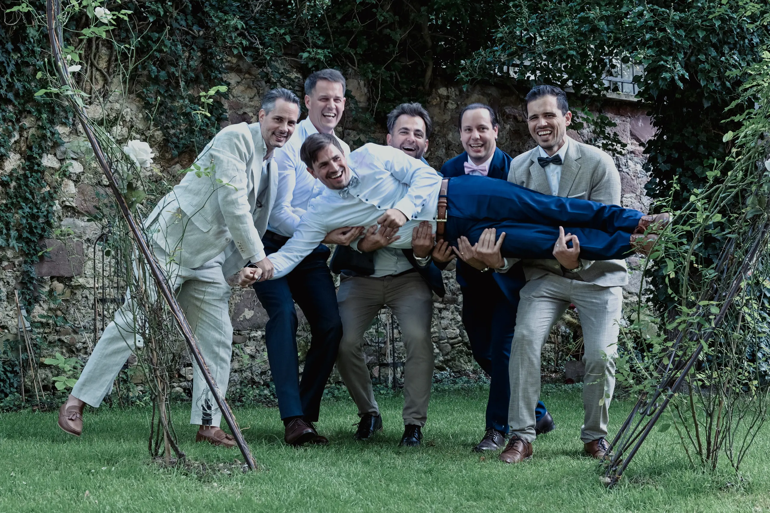 Fünf Männer werfen den Bräutigam lachend in die Luft.