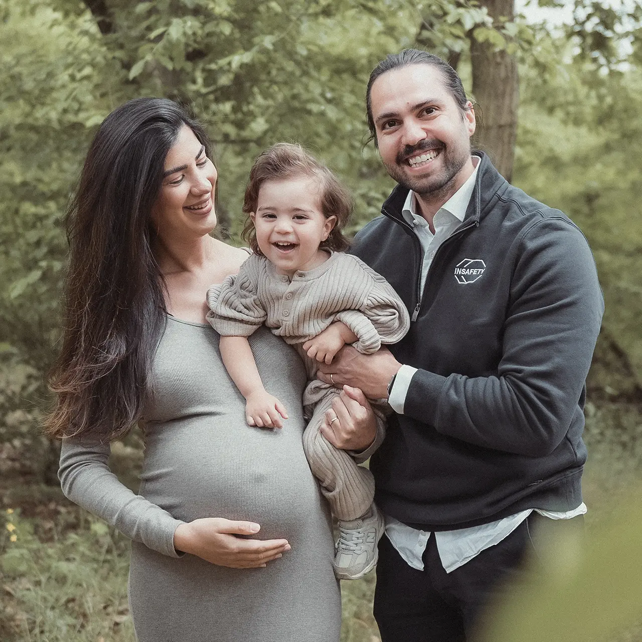 Lachendes Familienfoto mit Babybauch im Grünen.